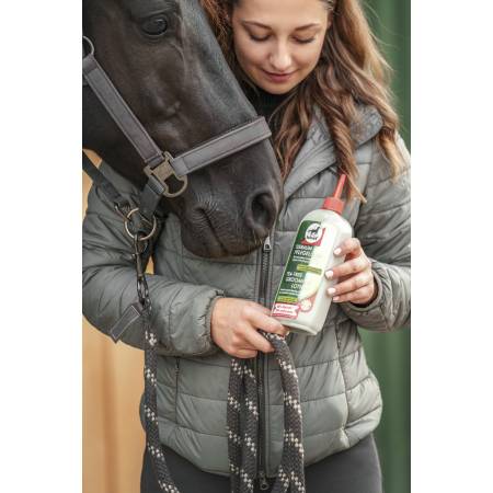 Cavalier tenant un flacon de lotion de soins Arbre à Thé Leovet devant la tête d'un cheval